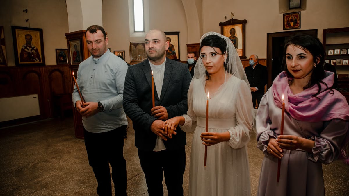 A serene Orthodox wedding ceremony featuring a bride and guests holding candles in a church.